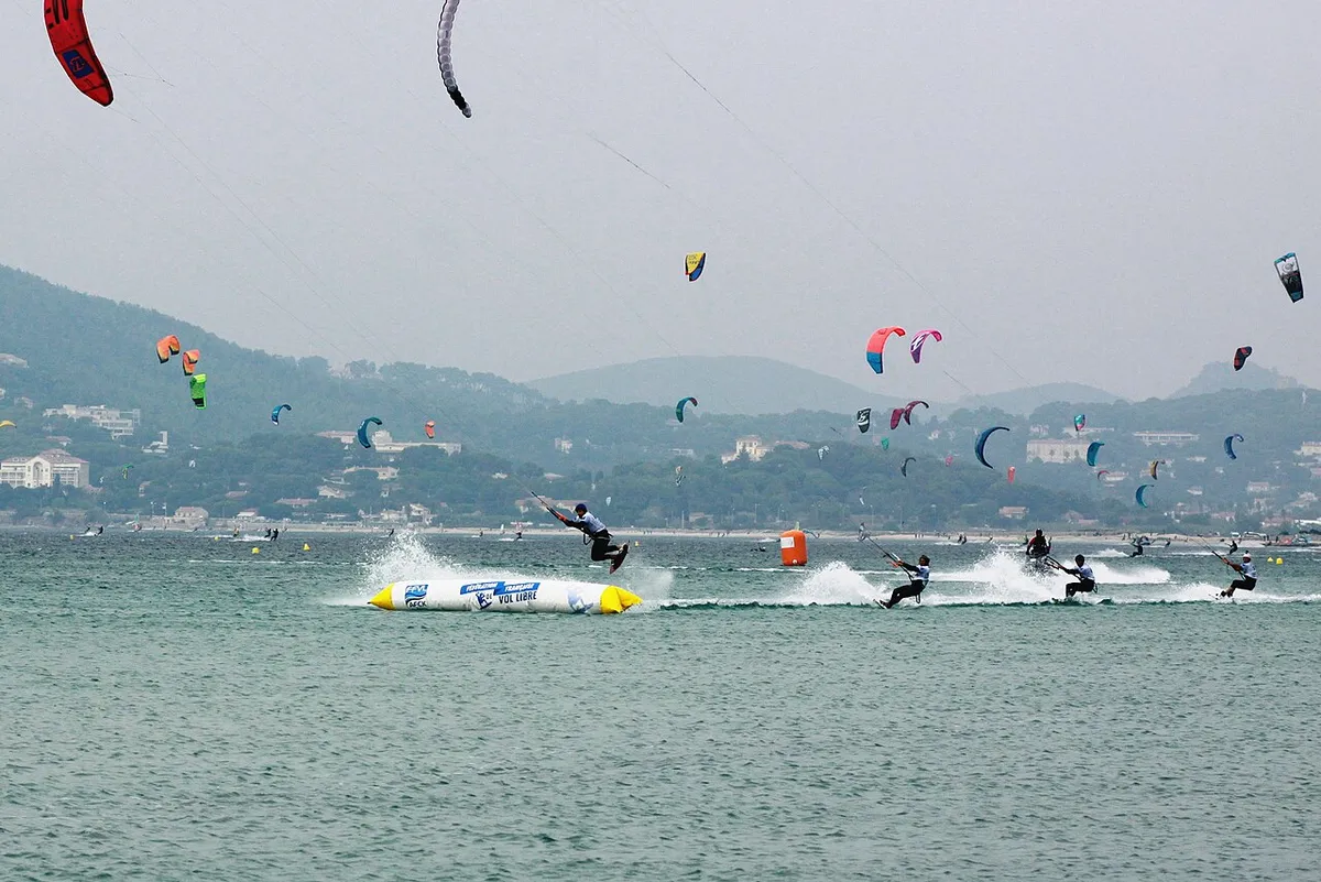 Kitesurfeurs en course dans la baie, avec une bouée gonflable jaune et de nombreuses ailes dans le ciel