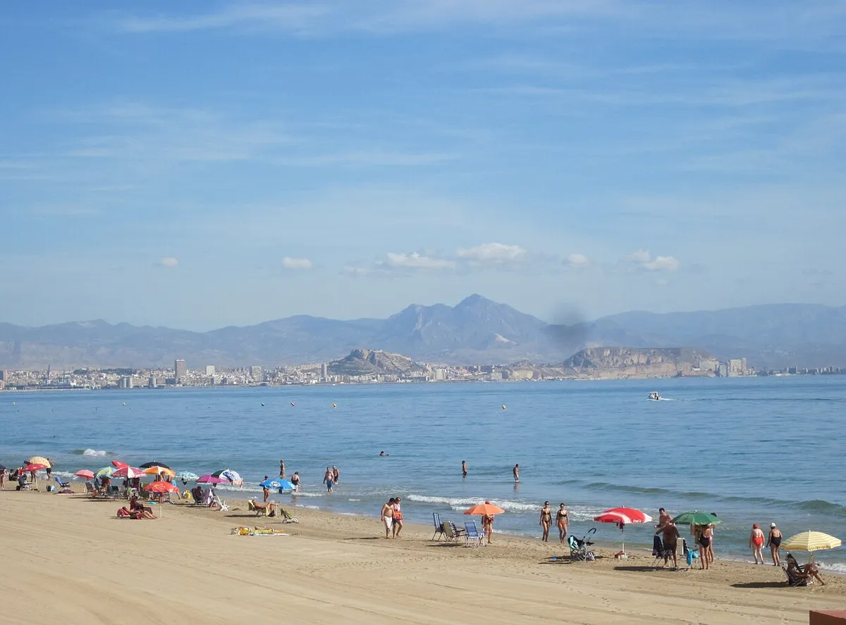Playa de arena de Arenales del Sol con sombrillas y bañistas, y la bahía de Alicante al fondo