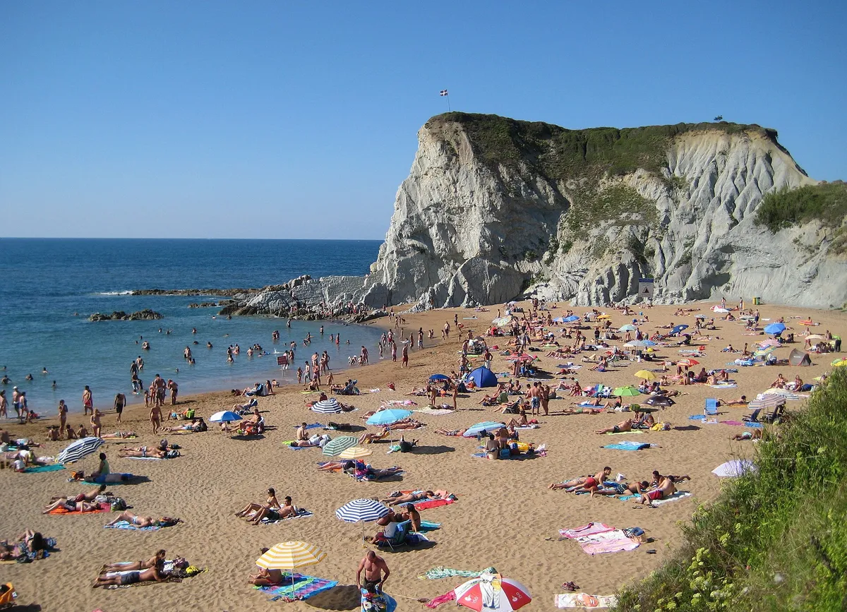Playa de Atxabiribil con muchos bañistas en la arena y un acantilado claro sobre el mar