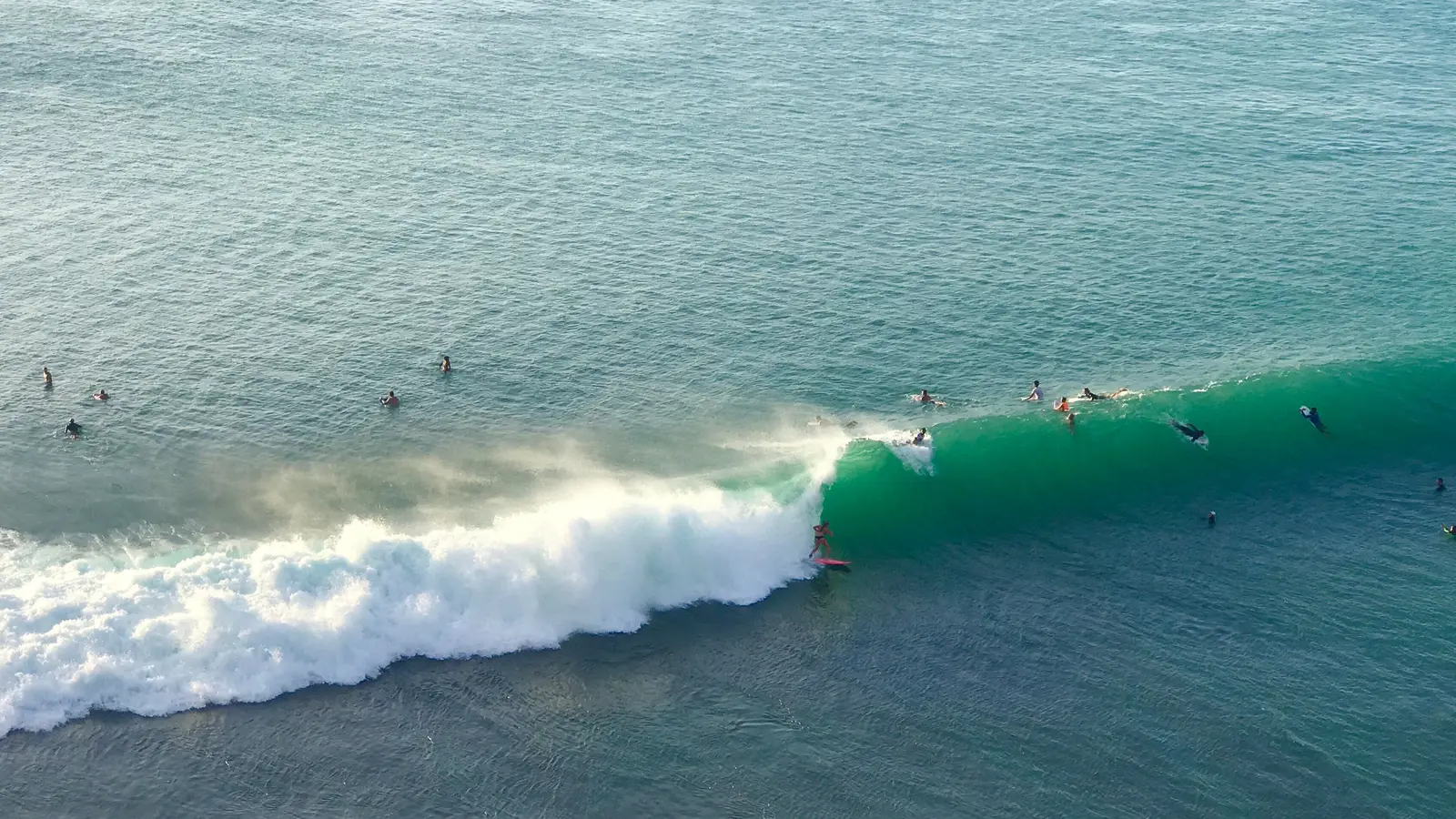 Surfers waiting and one riding a breaking reef wave in South Kuta district, on Bali's Bukit peninsula, seen from above