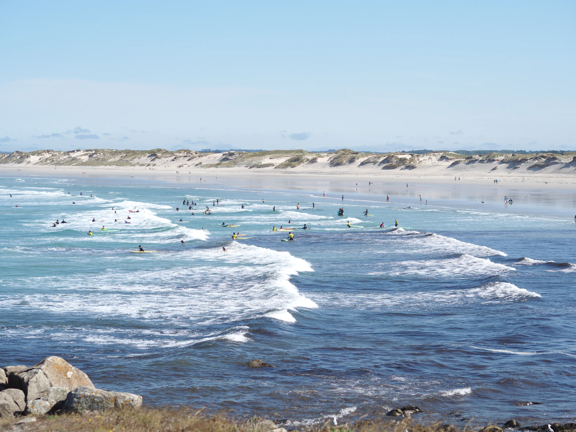 Nombreux surfeurs dans les vagues à La Torche, avec les dunes de Pors Carn en arrière-plan