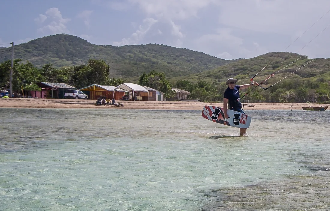 Kitesurfista llegando a la orilla frente al pueblo de Buen Hombre, colinas verdes detrás