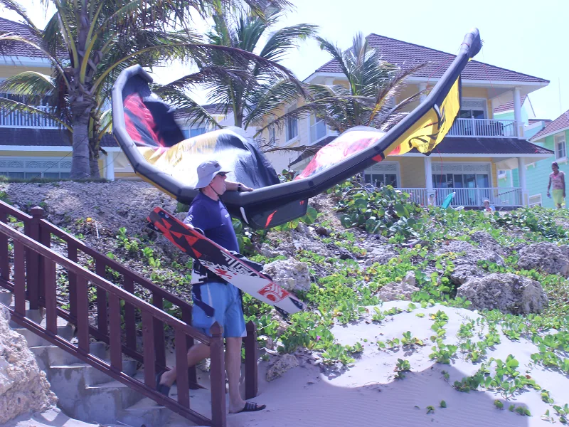 Kitesurfeur se dirigeant vers l'eau, aile et planche sous le bras, devant les villas pastel de Cabarete