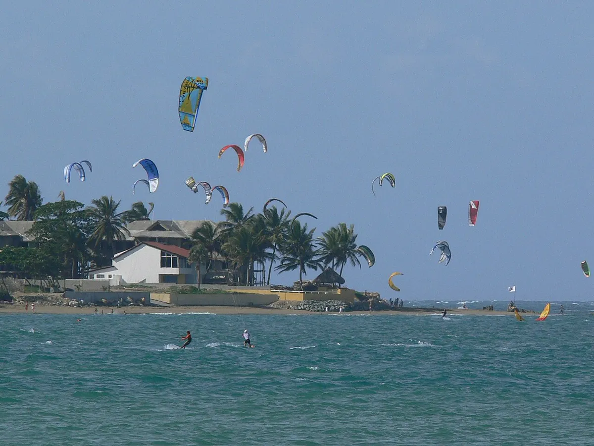 Kitesurfeurs et ailes dans le ciel devant la plage de Cabarete, palmiers et bâtiments en arrière-plan