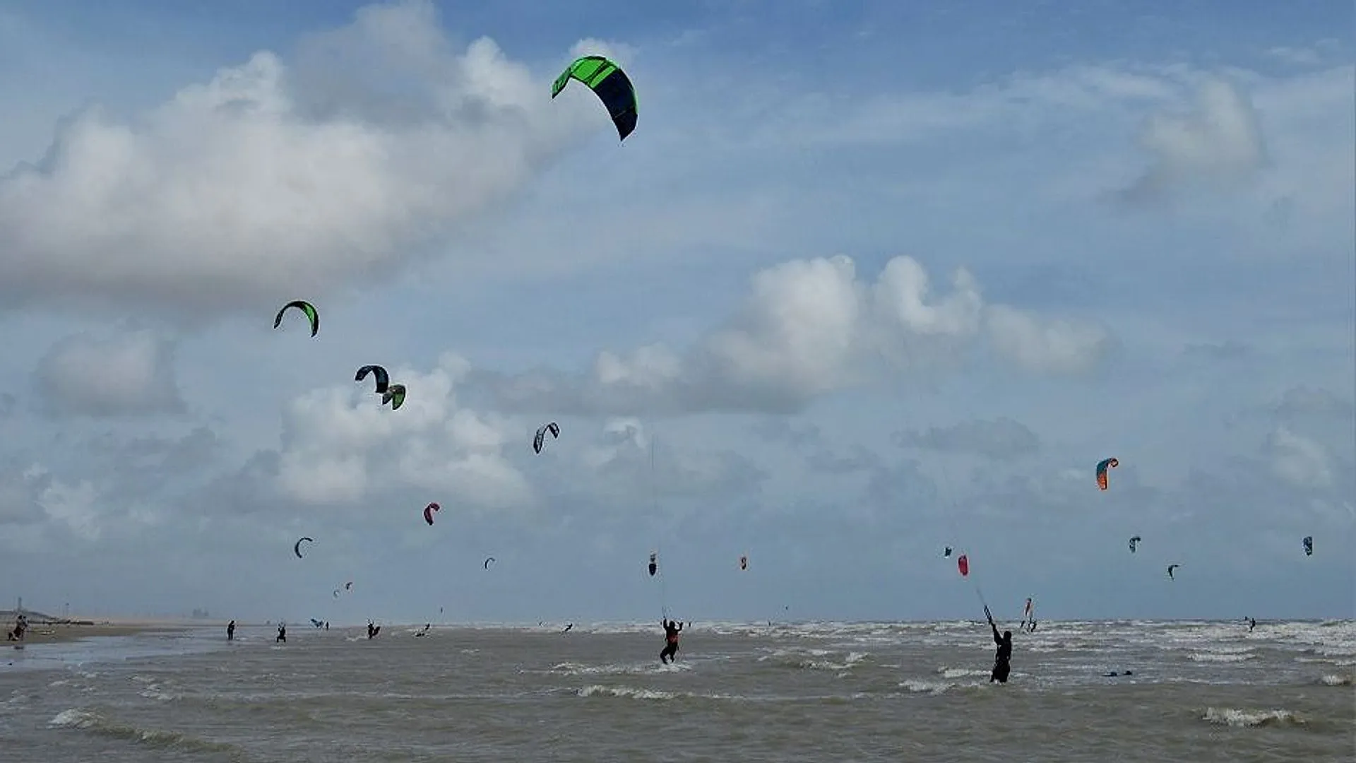 Kitesurfers and their kites over the surf on the beach at Camber Sands under a cloudy sky