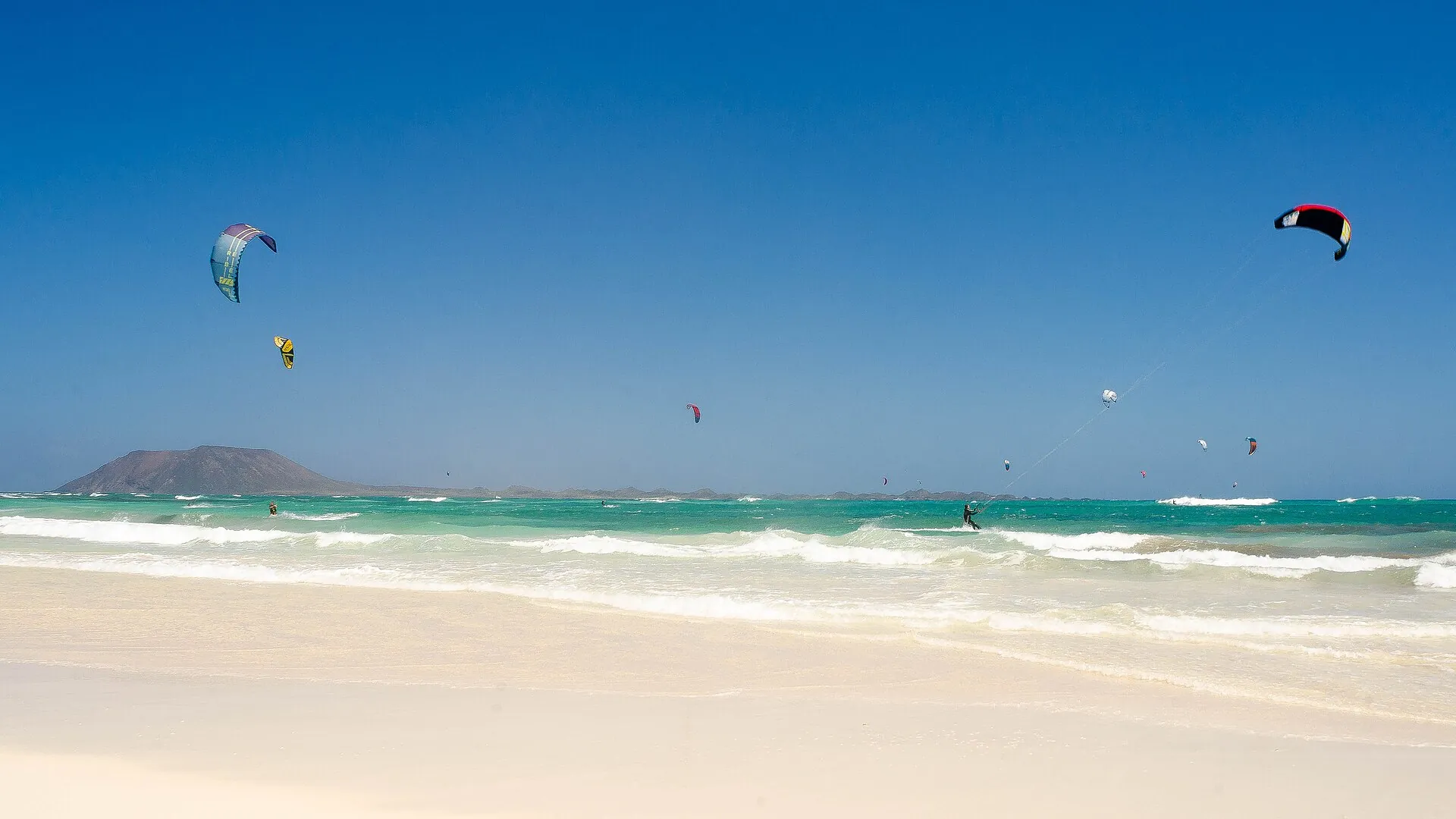 Kites over the sea and a white-sand beach at Flag Beach (Kite Beach), Corralejo, with the island of Lobos in the distance
