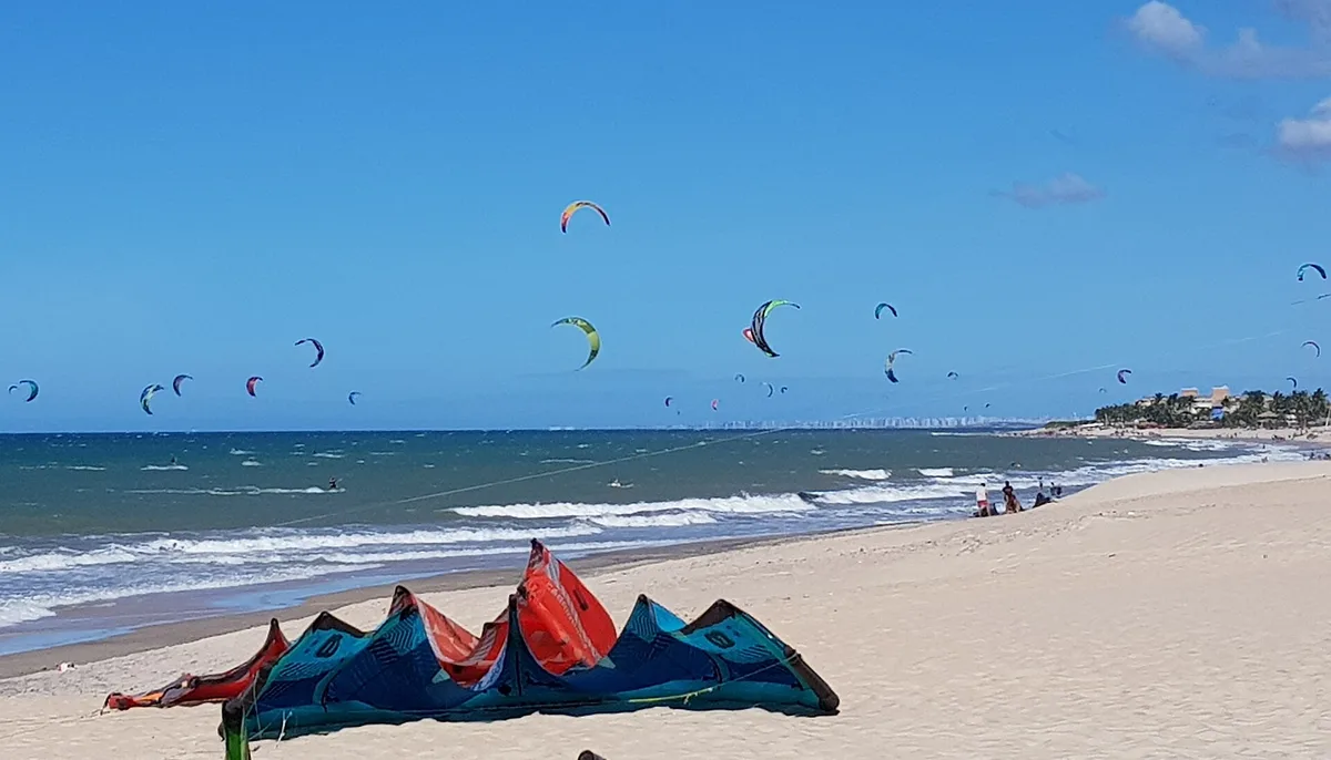 Kites laid out on the sand at Praia do Cumbuco, with dozens more flying offshore, Ceará, Brazil