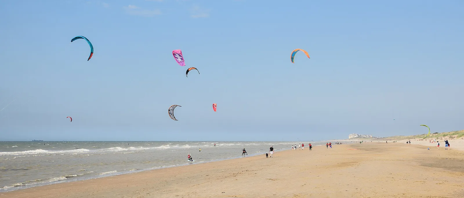 Plusieurs ailes de kitesurf au-dessus de la plage de De Haan, sur la côte belge, avec des promeneurs sur le sable
