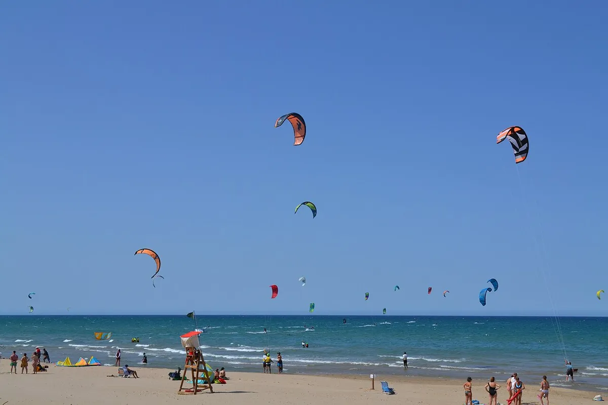 Cometas de kitesurf en el aire frente a la playa de Les Deveses, en Dénia, con una silla de socorrista en la arena