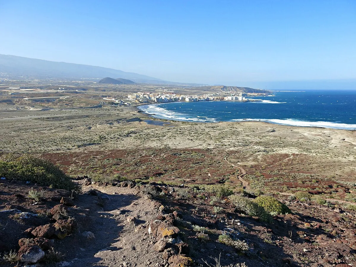 View over the bay and village of El Médano from the slopes of Montaña Roja, with whitecaps on a deep blue sea