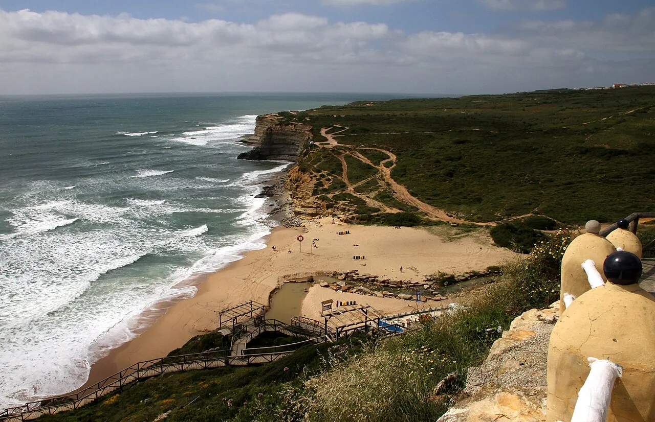Praia de Ribeira d'Ilhas seen from the cliff top, with the beach, the wooden walkways and waves breaking along the shore