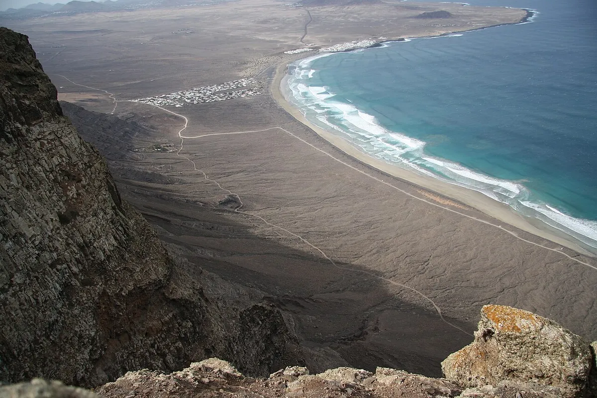 View down from the cliff edge over the long curve of Playa de Famara, with the white houses of the Famara urbanisation inland