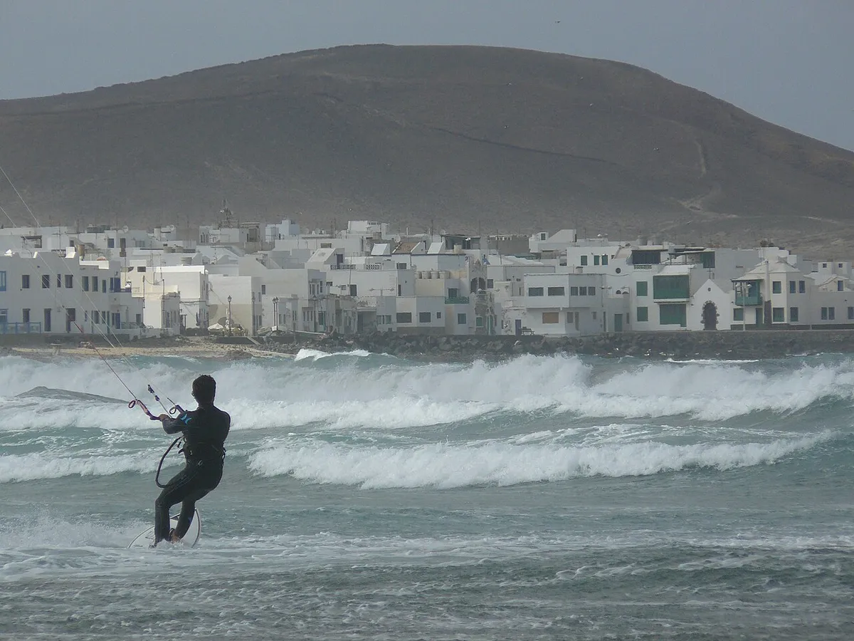 Kitesurfeur dans des vagues blanches devant un village de maisons blanches, plage de Famara, à Lanzarote