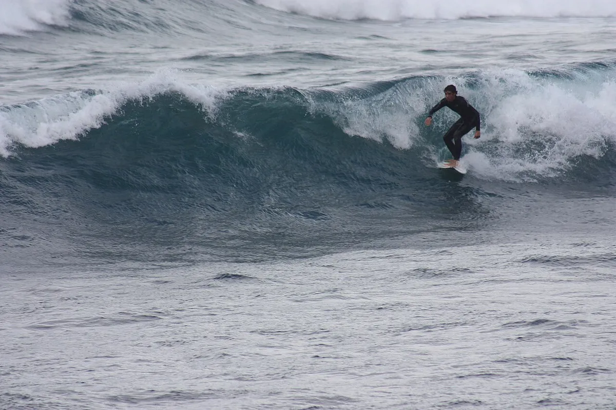 Surfer in a black wetsuit riding the face of a breaking wave at Caleta de Famara