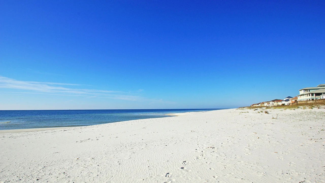 White sand and calm blue Gulf water at Gulf Shores, Alabama, with beachfront homes on the horizon
