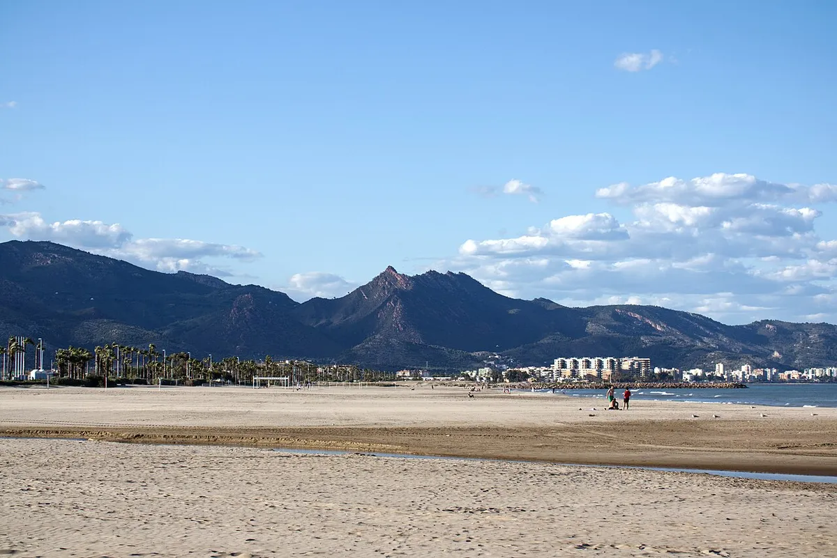 Playa de arena del Gurugú, en Castellón, con montañas y edificios al fondo