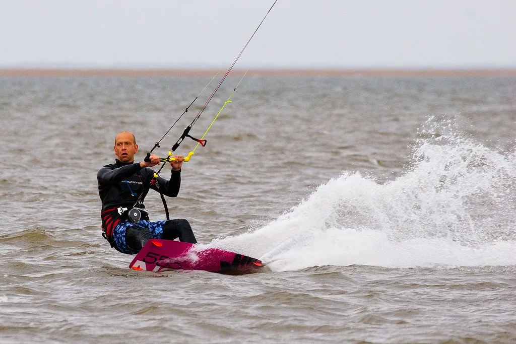 A kitesurfer throwing spray while riding the flat brown water of The Wash at Hunstanton, Norfolk
