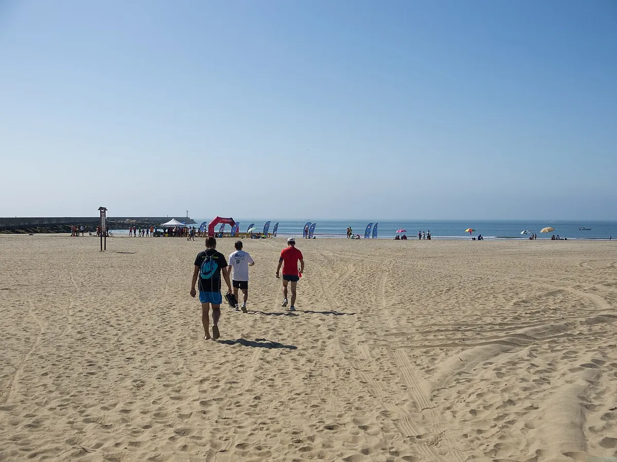Amplia playa de arena de Isla Canela con tres personas caminando y gente a lo lejos junto al mar