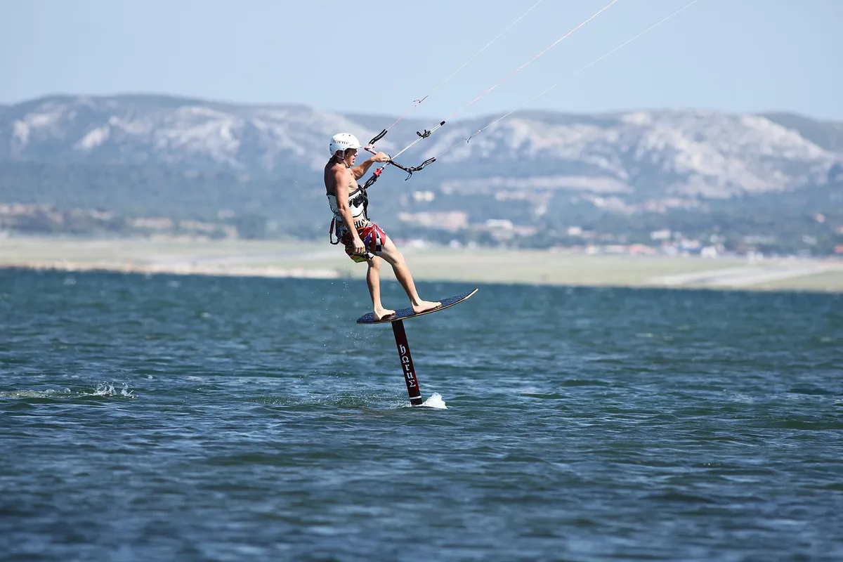 Piloto de kite foil con casco blanco y arnés, volando sobre el agua