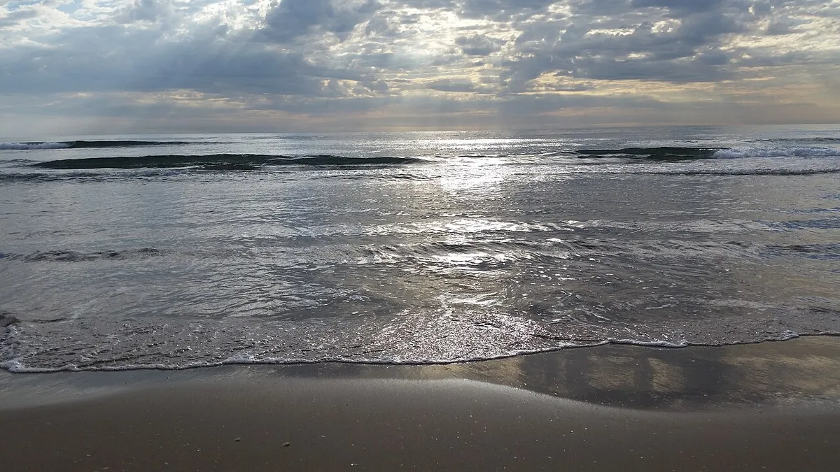 Olas con reflejos del sol entre las nubes en la orilla de la playa de Las Arenas, en Valencia