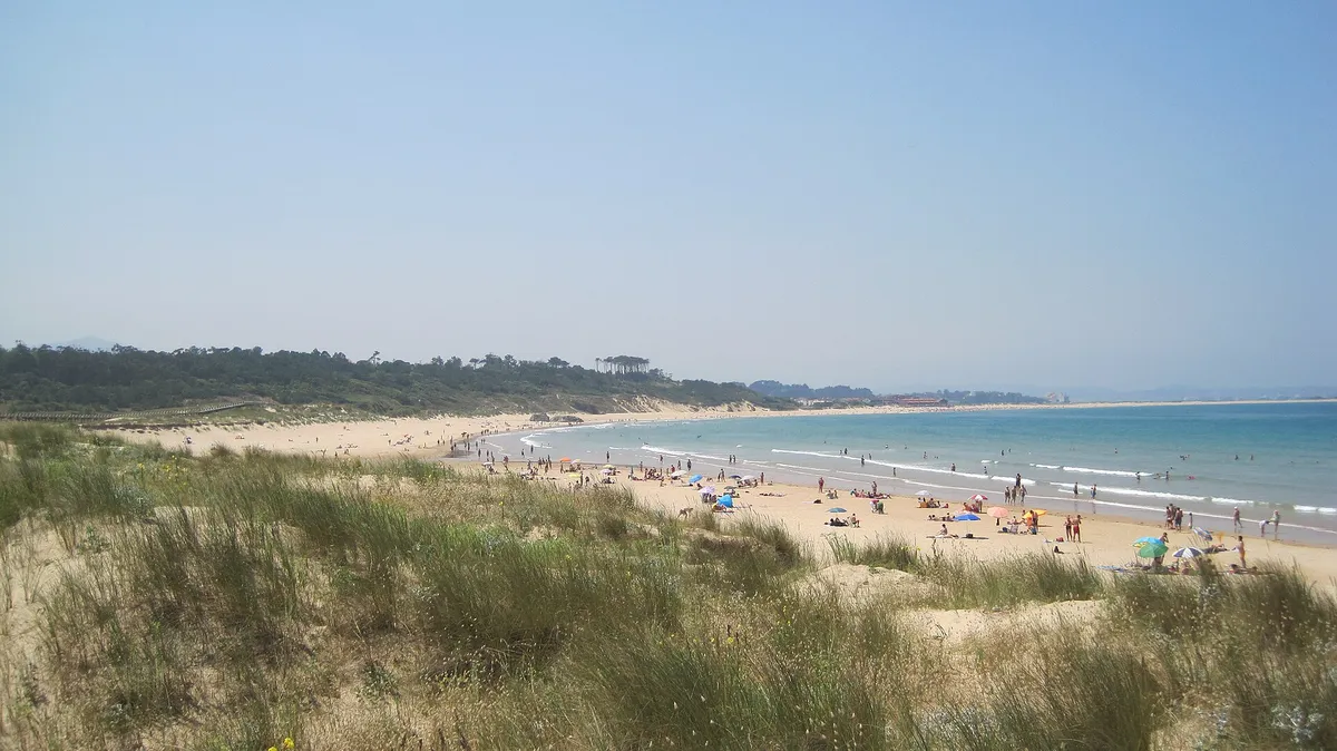 Playa de Loredo con dunas de arena y gente en la orilla bajo un cielo despejado