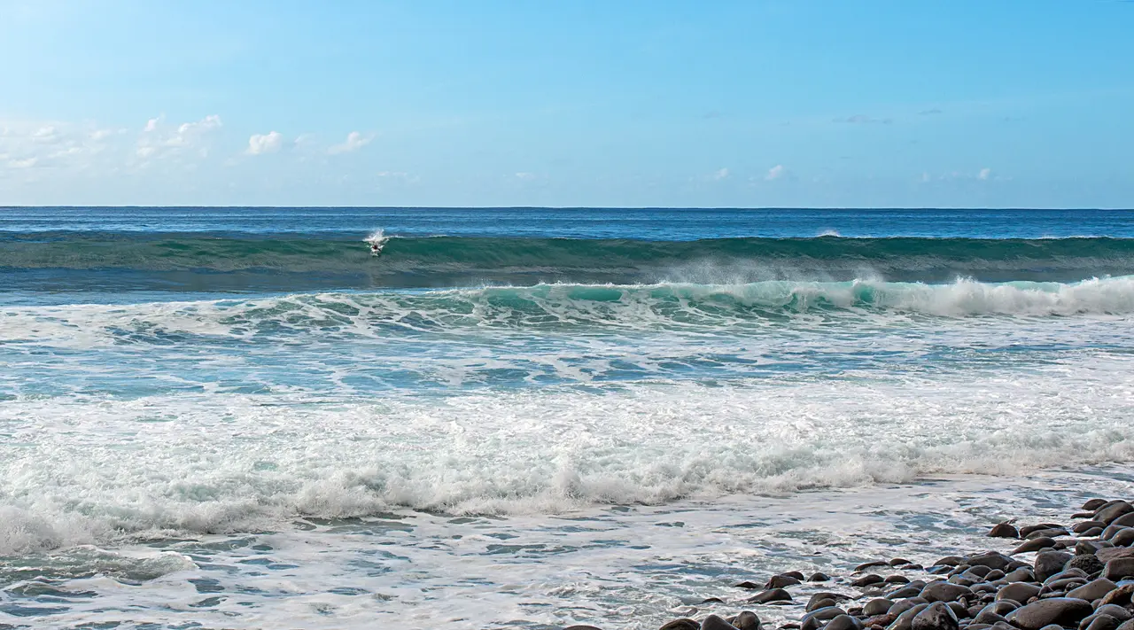 A surfer on a wave at Paul do Mar, Madeira, with whitewater rolling in towards a boulder shore
