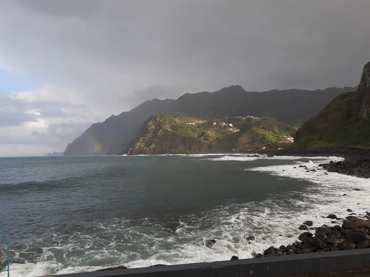 Waves washing onto the rocky beach at Porto da Cruz on Madeira's north coast, with green cliffs behind