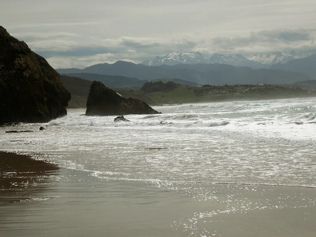 Playa de Merón con rocas, olas y montañas con nieve al fondo