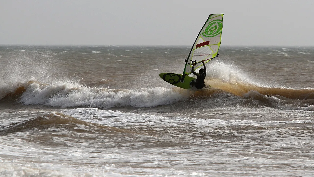 Windsurfista sobre una ola con vela verde y blanca en Moulay Bouzerktoun
