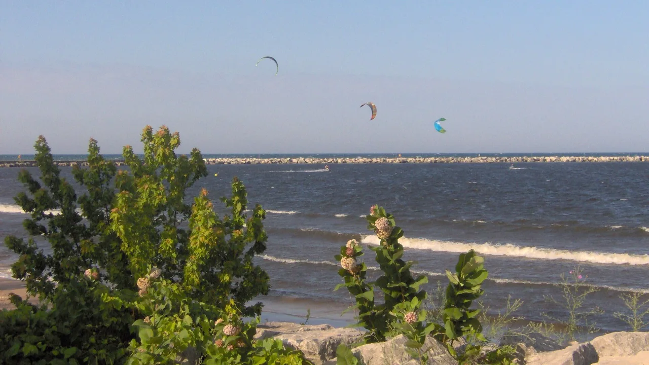 Three kiteboarding kites over Lake Michigan near a breakwater at Muskegon, Michigan, with small waves breaking in the foreground