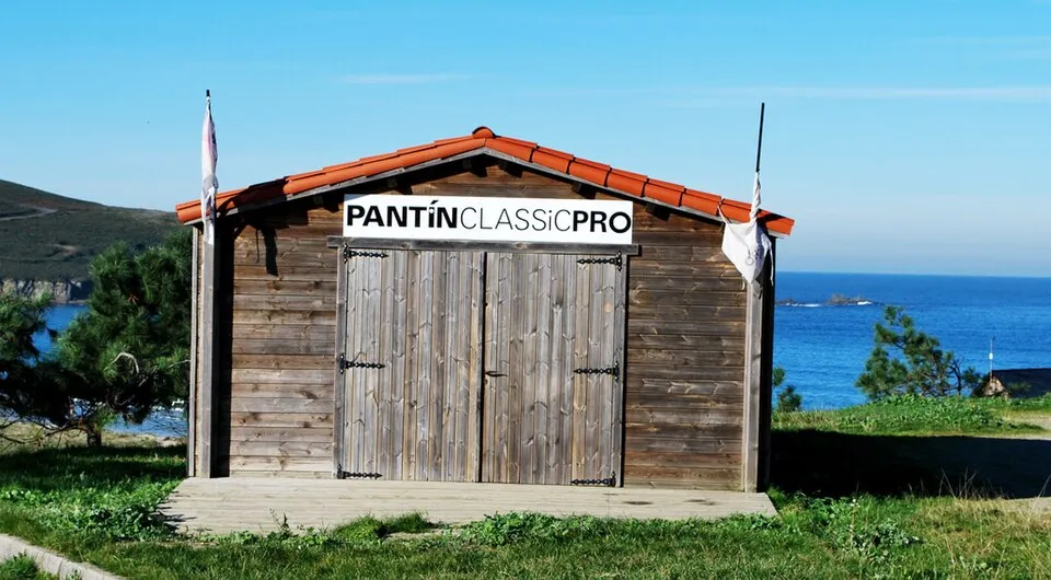 Caseta de madera con el rótulo «Pantín Classic Pro», junto al mar y entre pinos