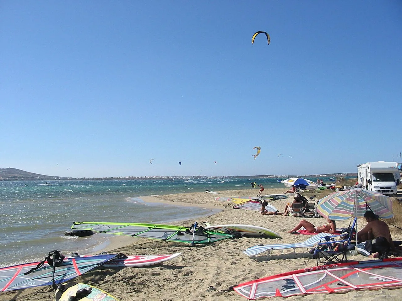 Kites in the air off Pounda beach, Paros, with windsurf sails laid out on the sand