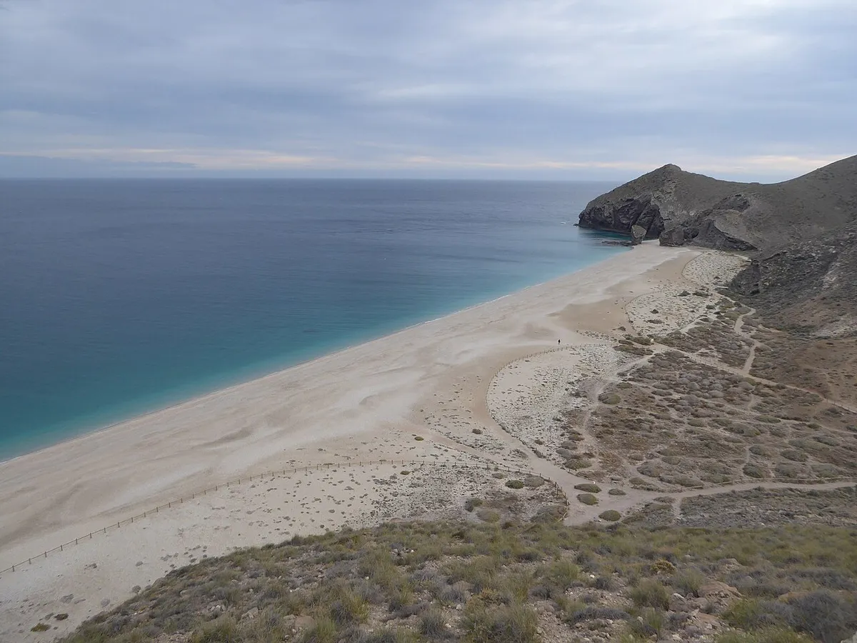 Vista desde lo alto de la playa de los Muertos: arena clara, mar azul turquesa y un cerro oscuro que entra en el agua