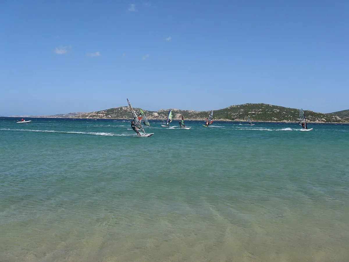 Windsurfistas sobre aguas turquesas en Porto Pollo, Cerdeña, con colinas al fondo