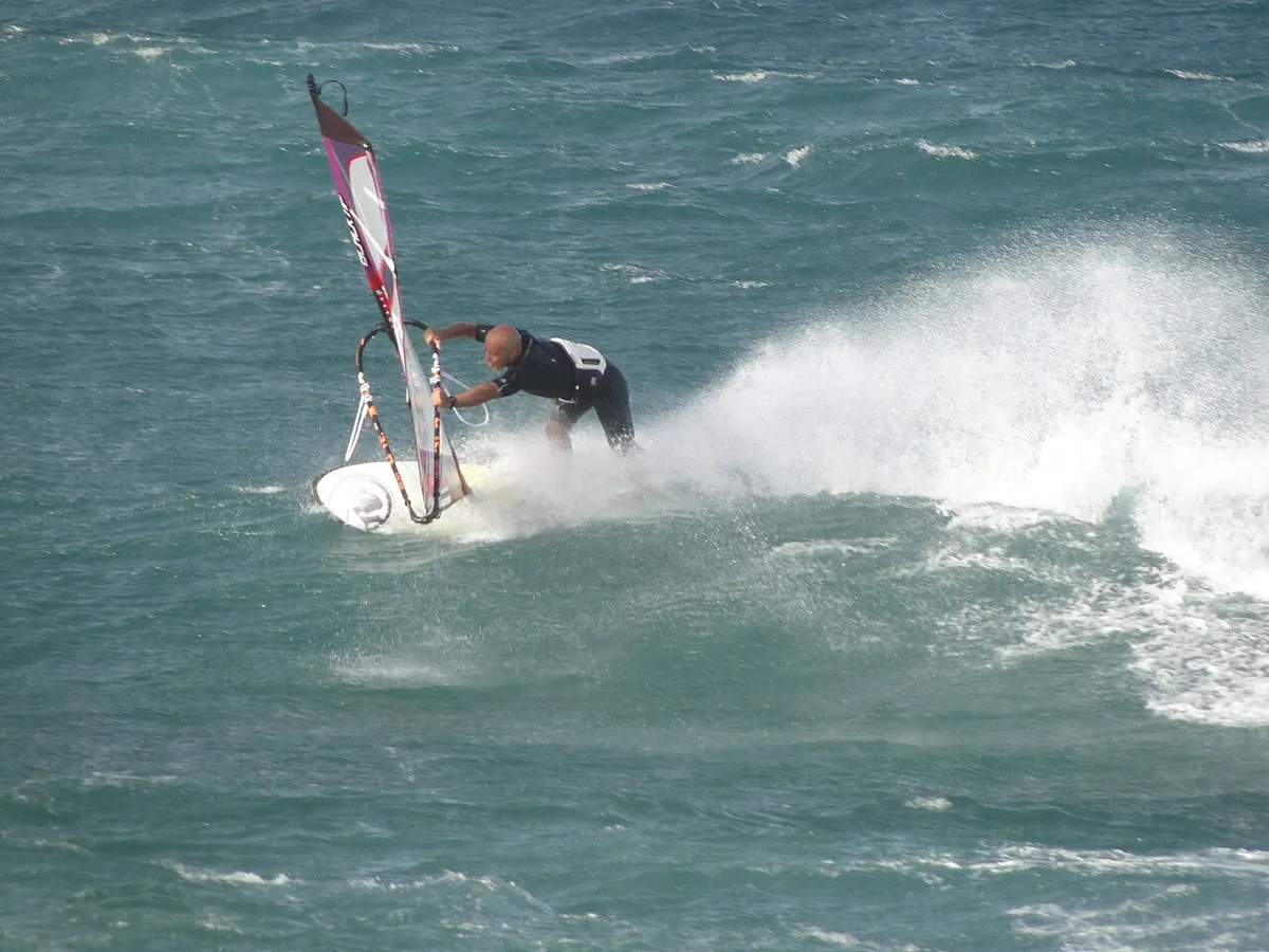 Windsurfista inclinado en un giro sobre una ola, con una nube de espuma detrás, en Pozo Izquierdo
