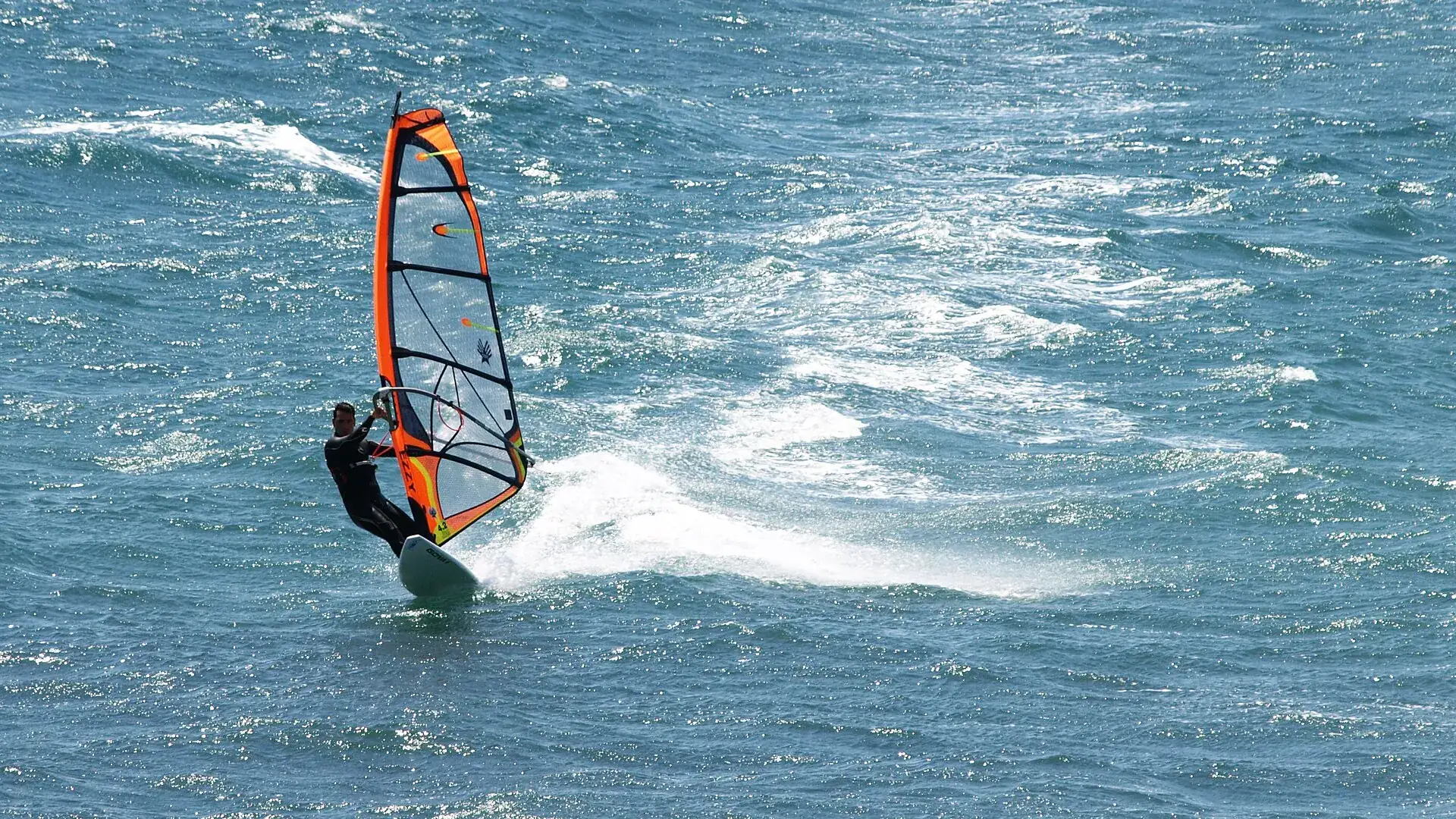 Windsurfista sobre agua picada, con espuma tras la tabla, en la playa de Pozo Izquierdo, Gran Canaria