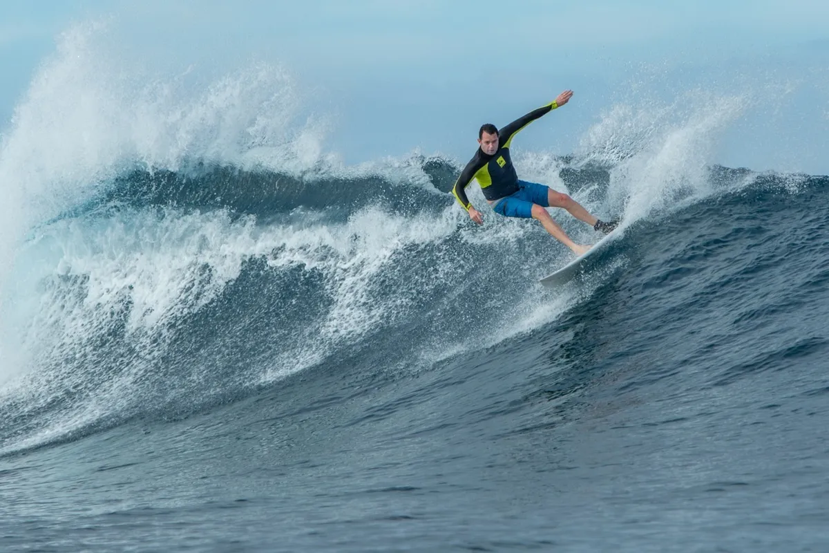 Surfeur qui prend un virage sur une grande vague bleue qui déferle, avec de l'écume projetée derrière lui