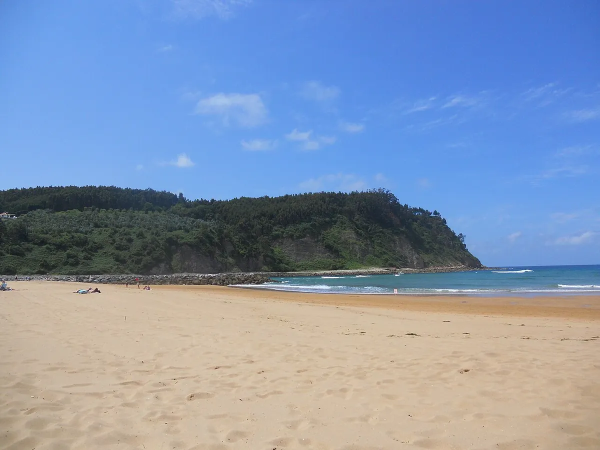 Playa de Rodiles, en Asturias: arenal amplio y, al fondo, una ladera arbolada junto al mar