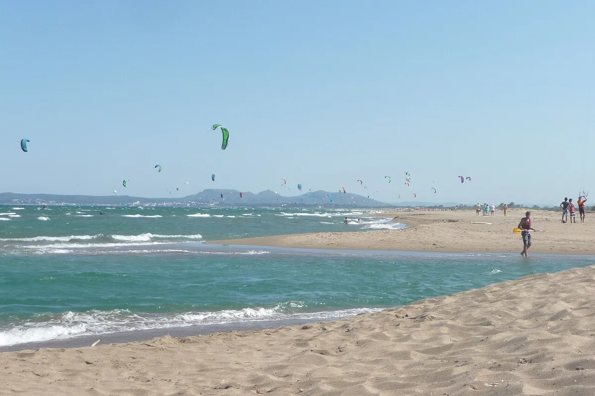 Kitesurfistas con cometas de colores en la playa de Sant Pere Pescador, con una lengua de arena y agua turquesa en primer plano