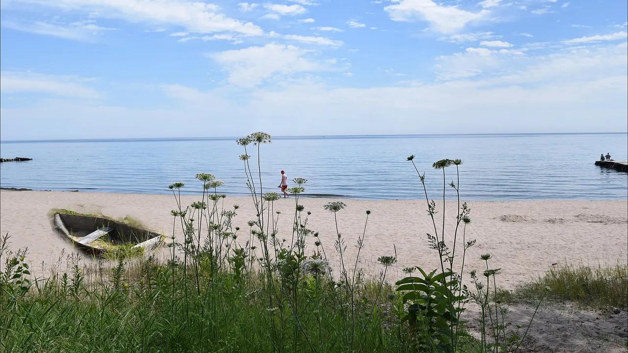 A calm summer afternoon on the Lake Michigan beach near downtown Sheboygan, Wisconsin, with a rowboat pulled up on the sand and a person walking along the shore