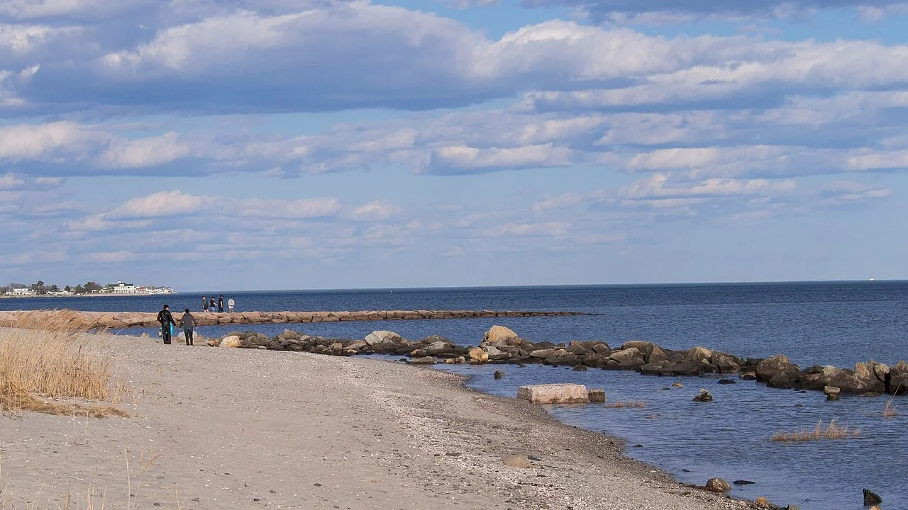 Calm water and a stone jetty at Silver Sands State Park, Connecticut, with people walking along the beach