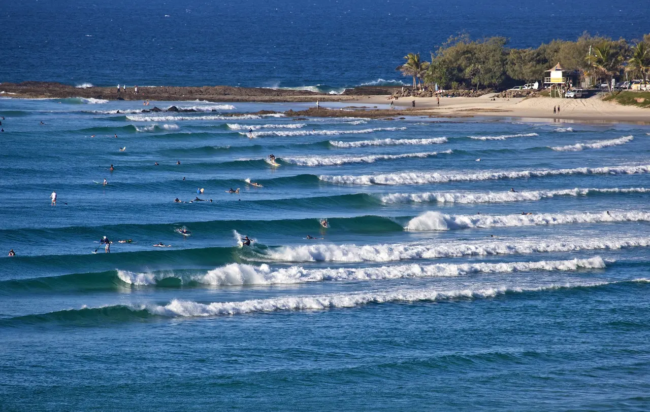 Surfers spread across lines of small waves wrapping around the point at Snapper Rocks, Gold Coast, with a lifeguard tower on the beach