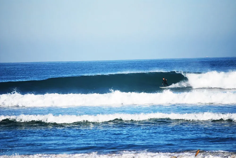 Ola rompiendo con un surfista en ella, frente a la arena de la playa