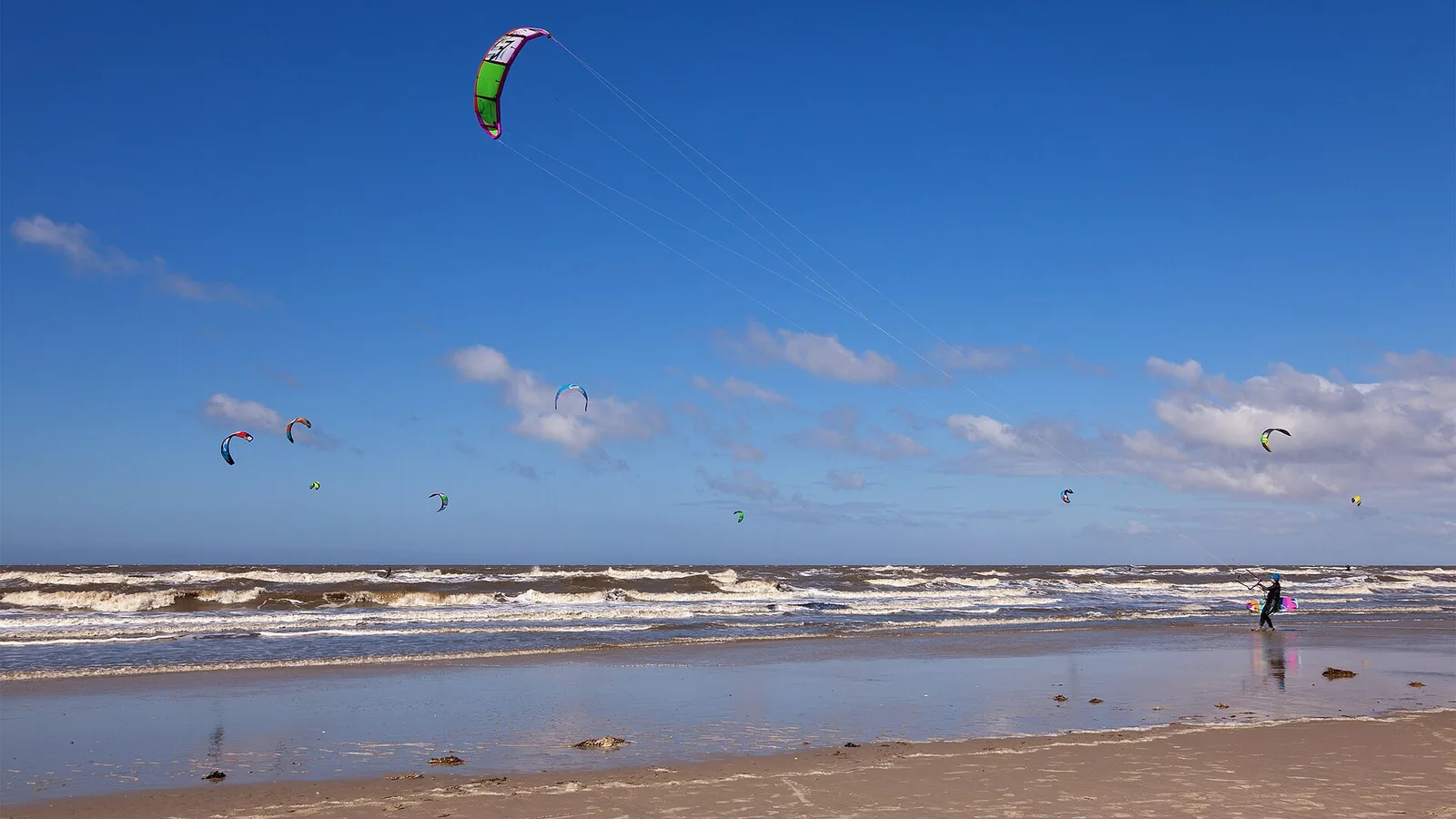 Ailes de kitesurf au-dessus de la plage de St. Peter-Ording, avec un kitesurfeur qui marche au bord de l'eau