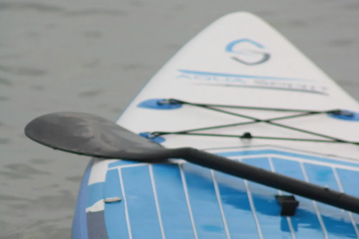 Primer plano de la punta de una tabla de paddle surf azul y blanca con el remo apoyado encima