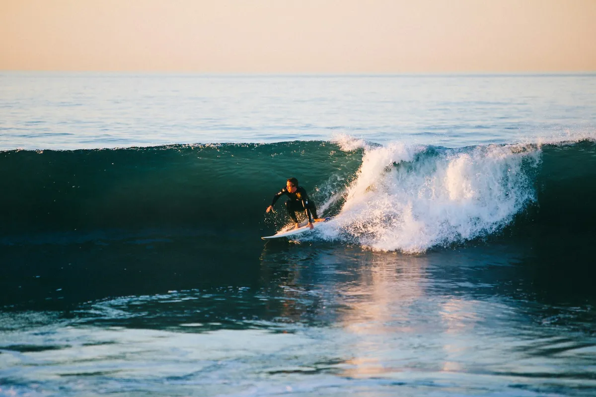 Surfer in a black wetsuit crouched low on the board, knees bent, on the face of a wave