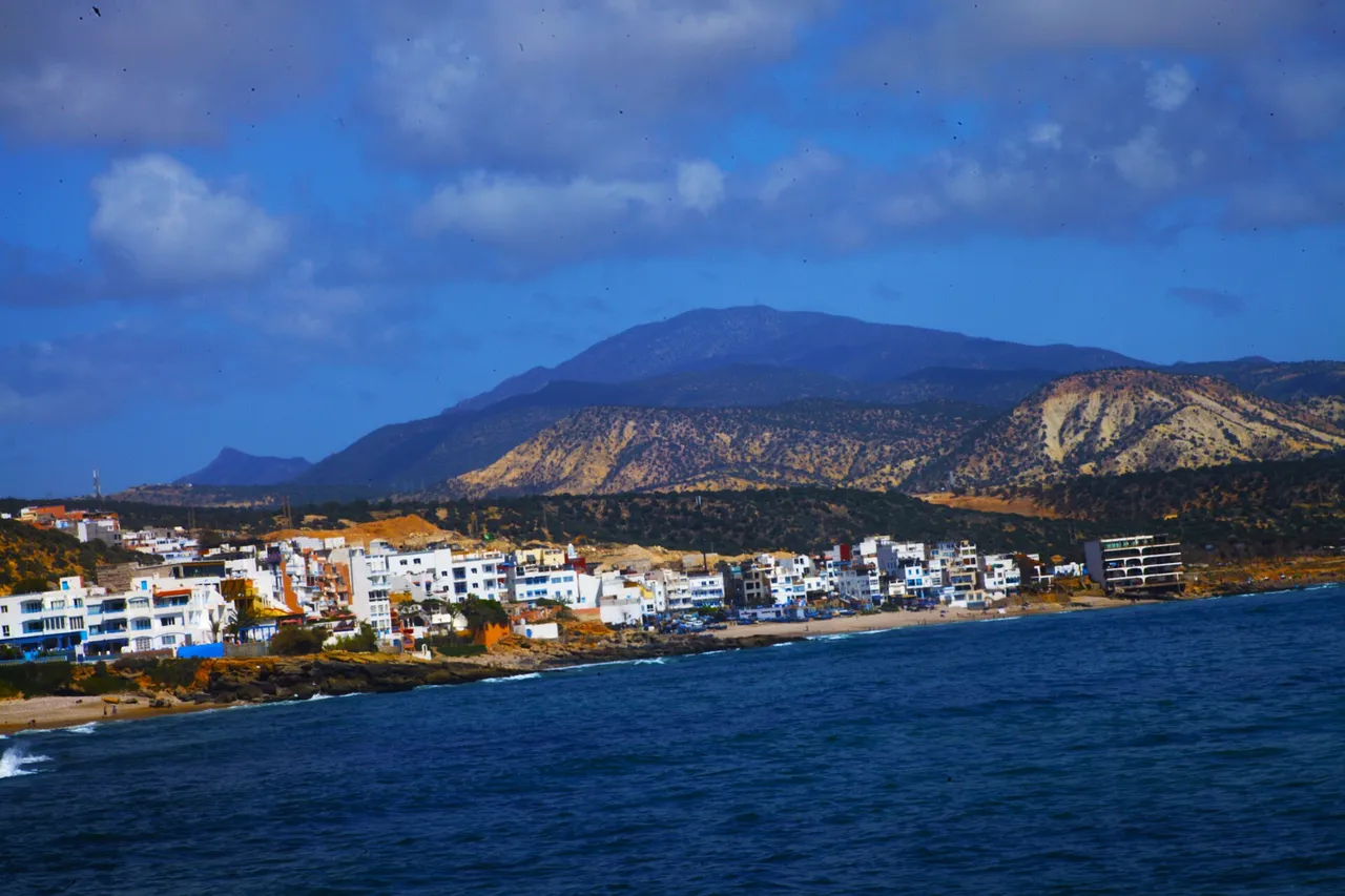 Les maisons blanches de Taghazout au bord de l'eau, avec des collines arides et des montagnes en arrière-plan