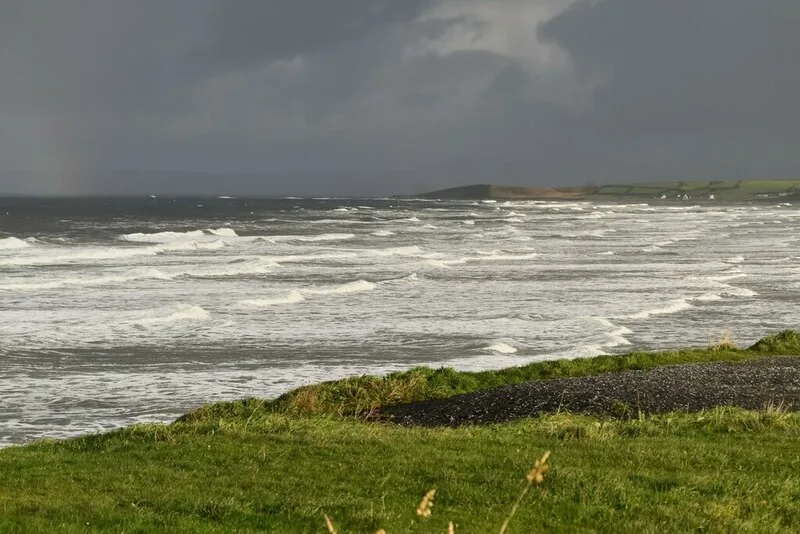 Rows of white water rolling into Tullan Strand near Bundoran under a dark sky, seen from the grassy clifftop