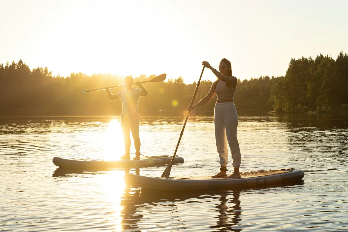 Two paddlers standing on stand-up paddle boards on calm water in low sun