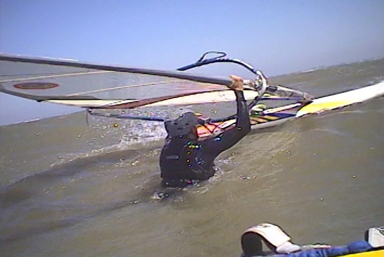 A windsurfer in the water lifting the sail clear of the surface at the start of a waterstart